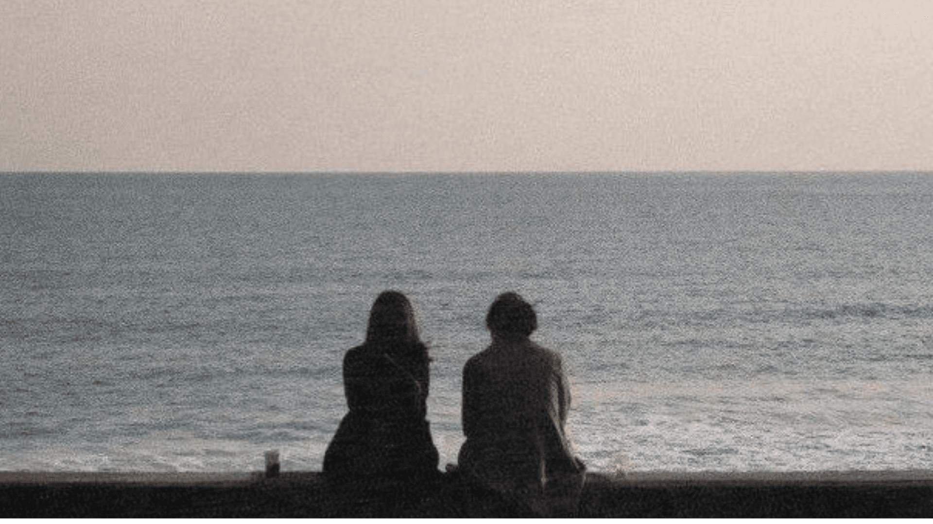 casal sentado, olhando para o oceano